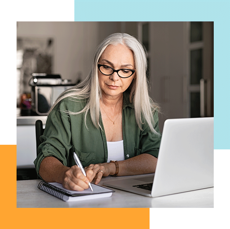 A woman writing on her notebook, next to her laptop.