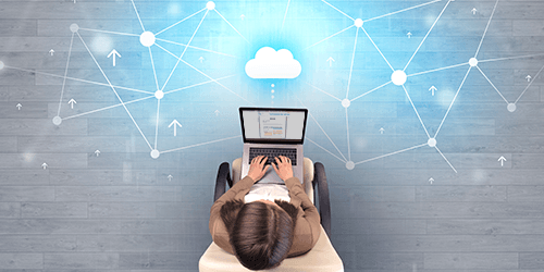 An overhead view of a woman on a laptop with a cloud projected above the laptop.